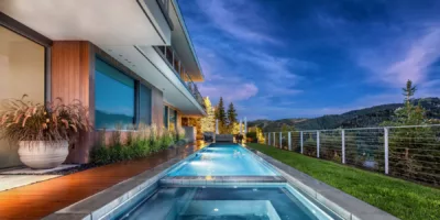 Swimming Pool with spa pool next to large house overlooking hillside at night - Precision Pools